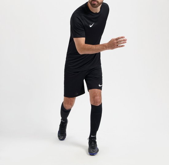 Homme barbu en mouvement, portant un t-shirt de sport noir, un short noir, des chaussettes noires et des chaussures de football.