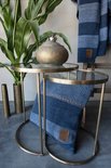 Blauw en grijs gestreept kussen op een glazen tafel, met een blauwe plaid erachter.