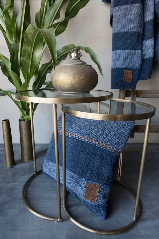 Blauw en grijs gestreept kussen op een glazen tafel, met een blauwe plaid erachter.