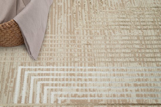 Beige en bruin vloerkleed met geometrische lijnen en 3D-effect. Deels bedekt door een mand en deken.