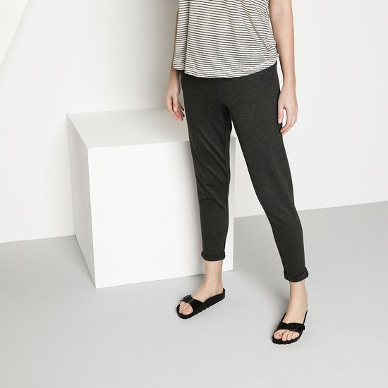 Model draagt zwarte Birkenstock slippers met gesp en een gestreepte top en donkere broek.