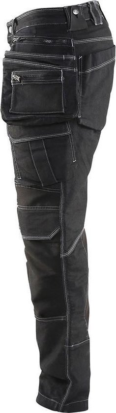 Zijzicht van een zwarte werkjeans met vele zakken, gespen en witte stiksels.