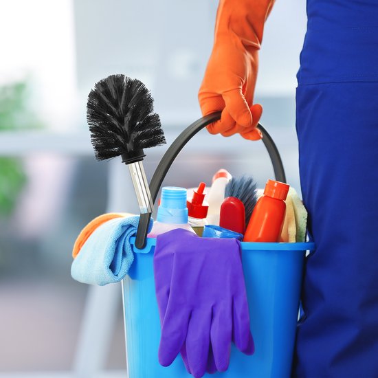 Hand met oranje handschoen die een blauwe emmer met schoonmaakspullen vasthoudt, waaronder een toiletborstel.