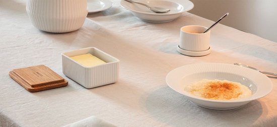Une table dressée avec de la vaisselle blanche en porcelaine, des bougies et un beurrier contenant du beurre.