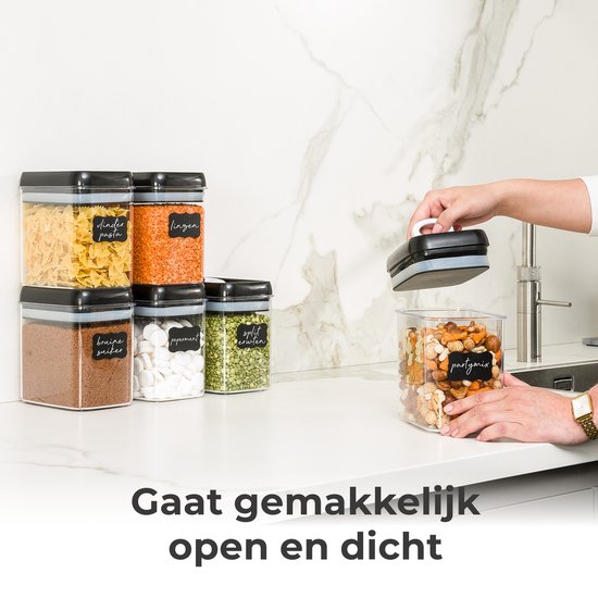 Pot de stockage transparent avec couvercle noir, rempli de mélange apéritif, ouvert facilement par une main.