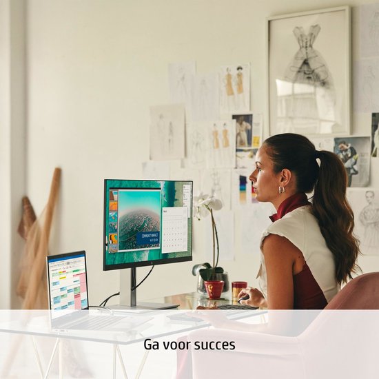 Vrouw met paardenstaart zit aan een bureau met een laptop en een grote monitor waarop Windows 11 te zien is. Tekst: "Ga voor succes".