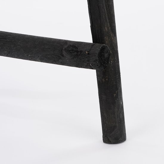 Close-up van de donkerzwarte, ruw afgewerkte houten voet en sport van een decoratieladder.