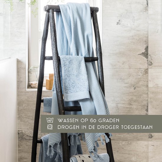 Lichtblauwe handdoeken hangen te drogen aan een donkere ladder in een badkamer. Tekst: WASSEN OP 60 GRADEN, DROGEN IN DE DROGER TOEGGESTAAN.