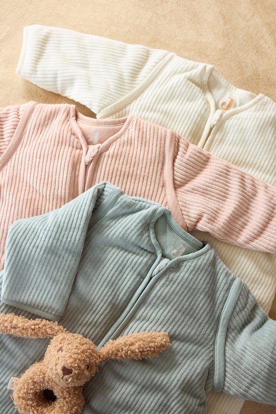 Drie baby slaapzakken in off-white, roze en lichtblauw, met naast een knuffel.