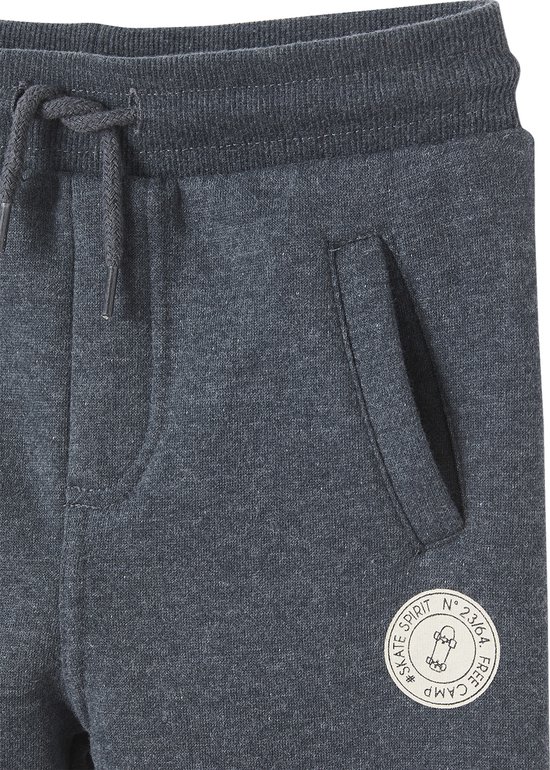 Detail van de tailleband van een donkergrijze joggingbroek met trekkoord, zak en rond logo met een skateboard.