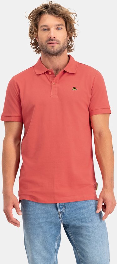Man met steil, golvend blond haar, een rood poloshirt met korte mouwen en lichtblauwe jeans.