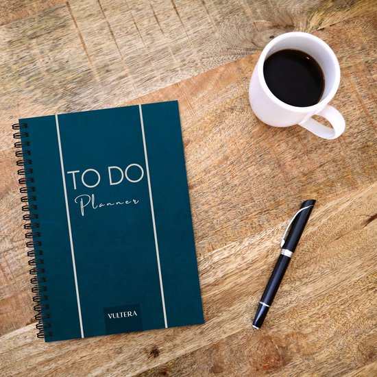 Blauwe 'TO DO Planner' met witte strepen, met pen en kopje koffie op houten tafel.