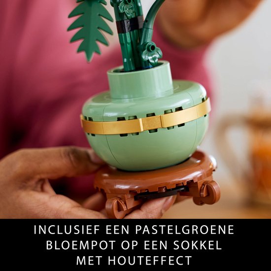 Gros plan du pot de fleurs LEGO vert pastel avec bande dorée et socle en bois.