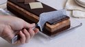 Zilverkleurige taartschep met een kat, die een plak chocoladetaart uitsnijdt.