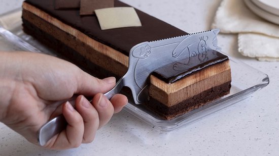 Zilverkleurige taartschep met een kat, die een plak chocoladetaart uitsnijdt.