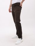 Man in bruine jeans, staand in profiel met hand in de zak.