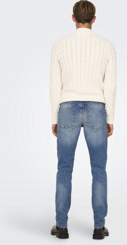 Man met een crème kabeltrui en blauwe jeans, achterkant.