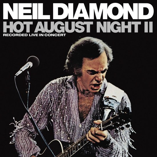 Neil Diamond live in concert, zingend en gitaar spelend in een glinsterend shirt.