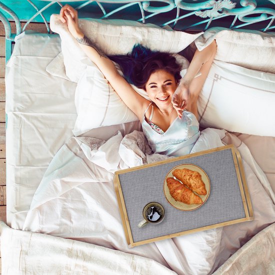 Vrolijke vrouw in bed met ontbijt op bed dienblad, met koffie en croissants.