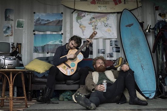 Twee mannen in een schuur, één speelt gitaar, de ander zit met een blikje.