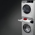 Witte AEG wasmachine en droger gestapeld met een witte lade ertussen, met rode en witte handdoeken erop.