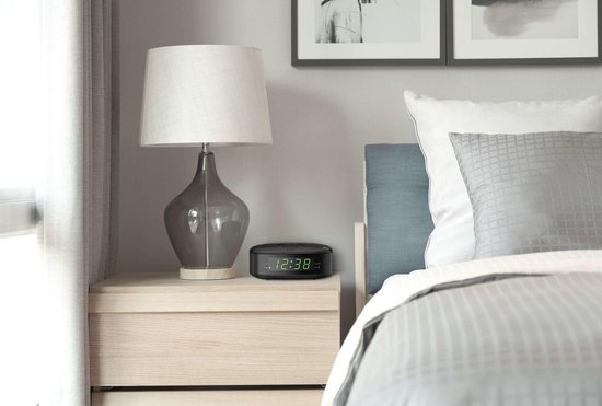 Zwarte Philips wekkerradio op een houten nachtkastje naast een bed.