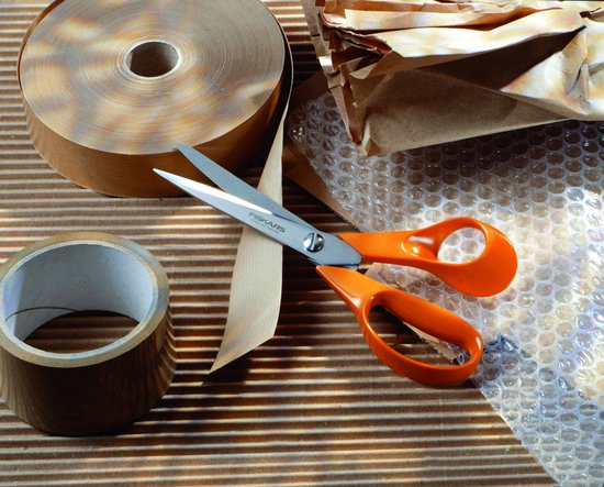 Oranje Fiskars schaar tussen rolletjes bruin inpakpapier en bubbeltjesplastic.
