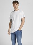 Man in wit t-shirt met kleine zwarte logoprint en jeans, hand in zak.