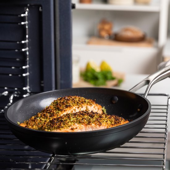 Gepaneerde vis in een zwarte KitchenAid-koekenpan op een ovenrooster.
