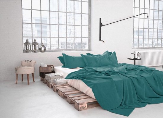 Chambre à coucher aménagée avec une literie vert émeraude, sur un lit fait de palettes.