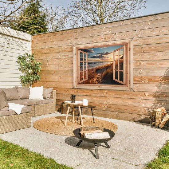 Tuinposter met houten raam, strand met duinen bij zonsondergang, in een buitenruimte met loungeset.