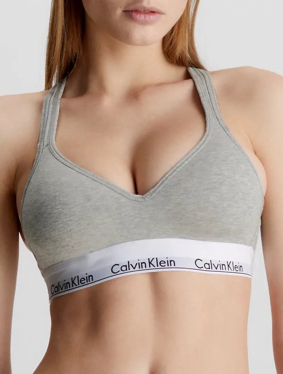 Model met grijze Calvin Klein bralette met diepe V-hals en witte band met logo.