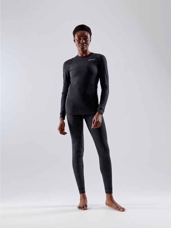 Vrouw draagt een donkergrijs thermoshirt en bijpassende thermobroek. Beide met subtiel logo.