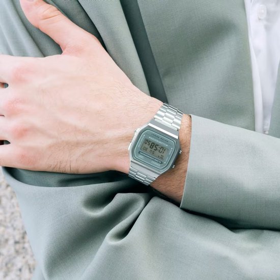 Zilverkleurig Casio horloge met groen digitaal display, gedragen om een pols onder een groen colbert.