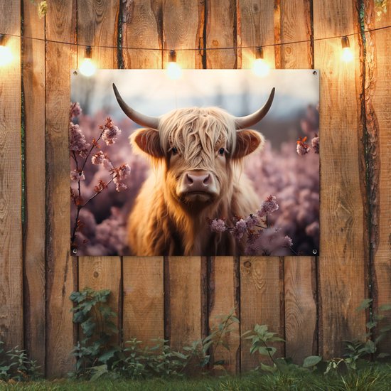 Tuinposter met Schotse hooglander in bloemen, hangend aan een houten schutting met lichtslinger.