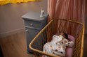 Baby in wit pakje slaapt in rieten wieg, met babyfoon op nachtkastje op achtergrond.