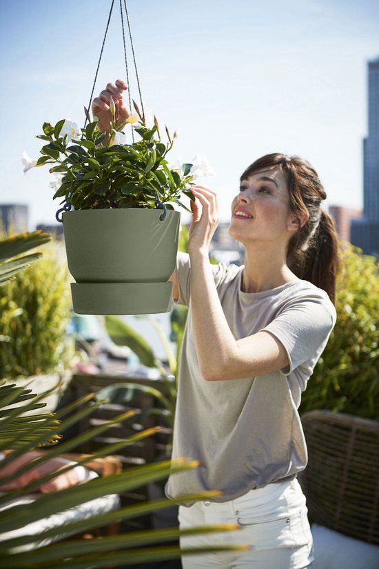 Vrouw met een grijze t-shirt en witte broek, verzorgt witte bloemen in een groene hangpot.