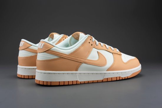 Een paar Nike Dunk Low damesschoenen, wit met oranje overlays, op een grijze achtergrond.