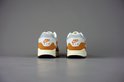 Achterkant van witte met oranje Nike Air Max 1 Patta sneakers met beige en bruine zolen. 'NIKE AIR' is zichtbaar.