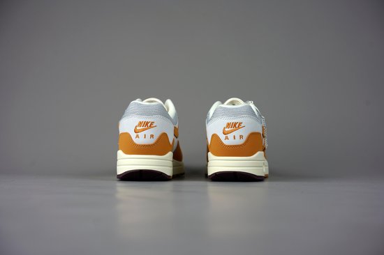 Achterkant van witte met oranje Nike Air Max 1 Patta sneakers met beige en bruine zolen. 'NIKE AIR' is zichtbaar.