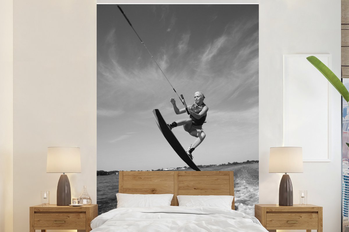 Behang - Fotobehang Een vrouw maakt een sprong in de lucht met haar wakeboard - zwart wit - Breedte 160 cm x hoogte 240 cm
