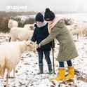 Twee kinderen met winterkleding en laarzen in de sneeuw, bij schapen.