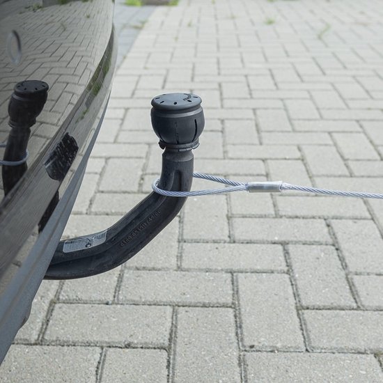 Zilverkleurige staalkabel met lus om de trekhaak van een zwarte auto, bevestigd op een betegeld oppervlak.
