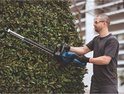 Man met veiligheidsbril en handschoenen snoeit struiken met een blauwe Bosch Professional accu heggenschaar.