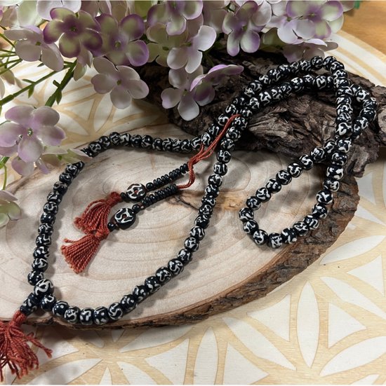 Zwarte gebedsketting met witte 'ohm' patronen, versierd met oranje kwastjes.