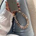 Gedetailleerde weergave van een champagnekleurig telefoonkoord met hartjesparels, bevestigd aan een telefoonhoesje.