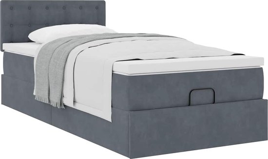 Donkergrijs bed met gestoffeerd hoofdbord, witte matrastopper en opbergruimte.