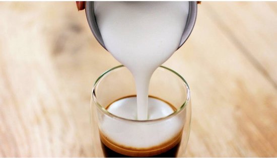 Zwarte melkopschuimer met romig melkschuim dat in een glas met espresso wordt gegoten.