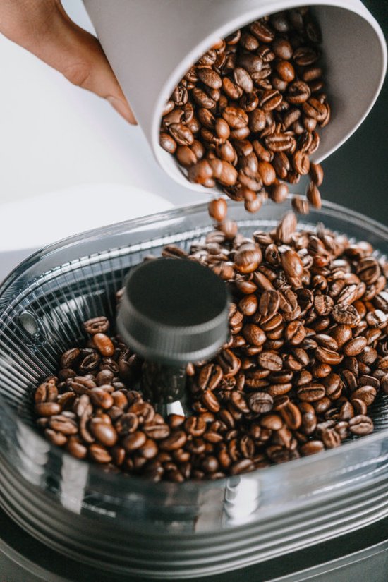 Koffiebonen worden uit een witte beker in de molen van een koffiezetapparaat gegoten.
