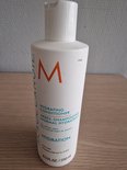 Witte Moroccanoil Hydrating Conditioner fles met oranje M-logo op een houten ondergrond.